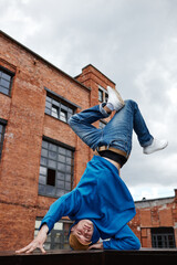 Vertical action shot of young man doing handstand breakdance pose in urban factory setting outdoor