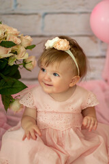 Fototapeta premium Pretty small girl with roses in beautiful dress sits and looks dreamy, beauty and fashion concept, indoor portrait against the backdrop of brick wall close-up. Beautiful little girl model .