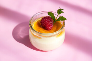 Creme brulee dessert decorated with fresh berries and mint leaf on a pink background with space for text. Sweet snack