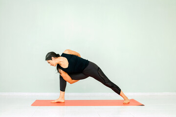 Hispanic mature woman performing asana exercises, workout routine. Black pants and top, studio background. Concept of yoga and wellness. Sports and healthy lifestyle.