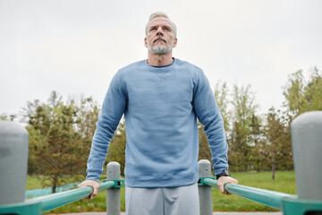 Low angle portrait of active mature man exercising on parallel bars outdoors, copy space