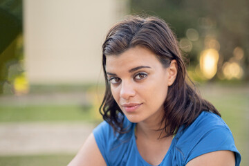 Portrait of a young Latin woman in a park looking at the camera. Honest and confident expression. Defocused background with bokeh balls.