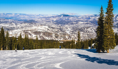 Fototapeta na wymiar View of ski slope near Aspen, Colorado, with ski tracks on foreground and mountain range in background on sunny winter day