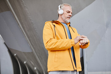 Waist up portrait of handsome senior man wearing headphones outdoors against concrete background in urban setting, copy space