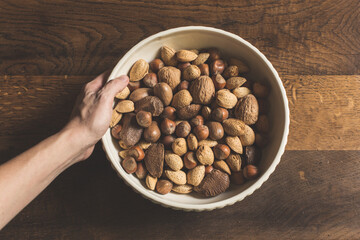Woman setting white ceramic bowl of mixed nuts on wood tabletop