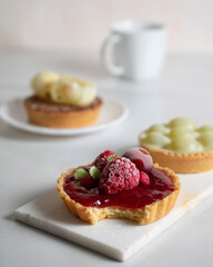 Small red berries pie bitten, on a white neutral background with a cup of coffee and two other smaller pies