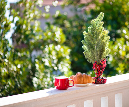 Christmas tree with a cup of tea and a croissant on the balcony against the backdrop of the forest