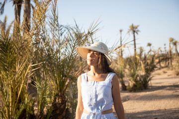 Tourist woman with hat walking through the desert landscape and palm trees that offers the city of Marrakech in its palm grove, this place is very visited in Morocco by tourists.