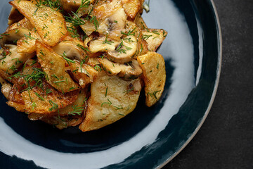 Fried potatoes with mushrooms on a dark background