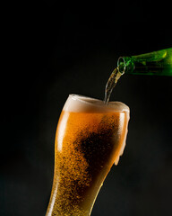 poring beer from a bottle into a tall glass with bubbles foam and a small splash
