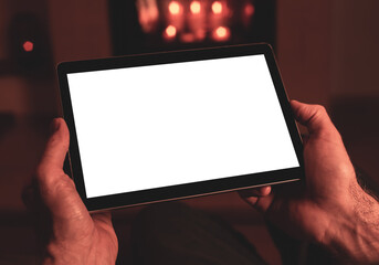 Man’s hands holding tablet with blank screen - background. Christmas mood, fireplace light. Free copy space.