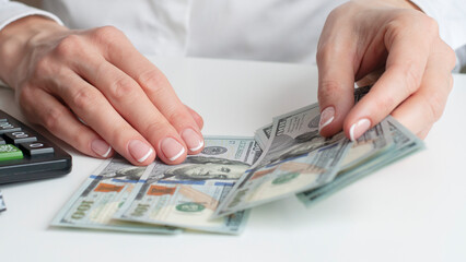 a man's hand holds out one hundred dollar bills against the background of an office table with a computer