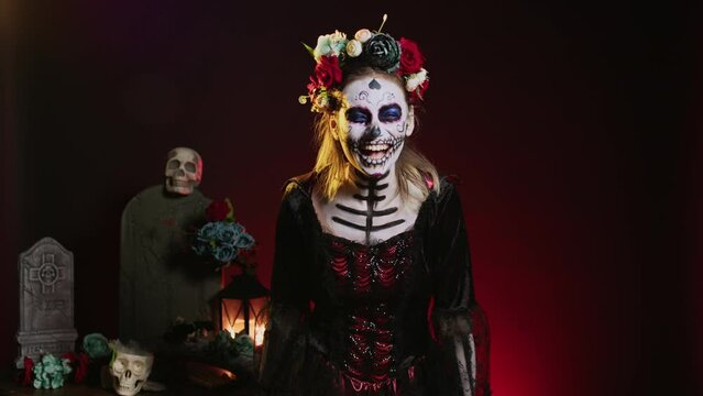 Scary loud goddess of dead yelling in costume with skull body art, wearing flowers crown and screaming like holy santa muerte to celebrate dios de los muertos. Woman on tranditional mexican holiday.