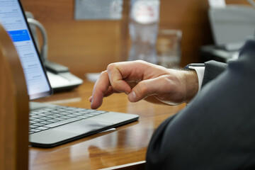 A man - an official, an accountant, a businessman or a lawyer, uses the touchpad of a small laptop while sitting at a table in the office. No face. Selective focus