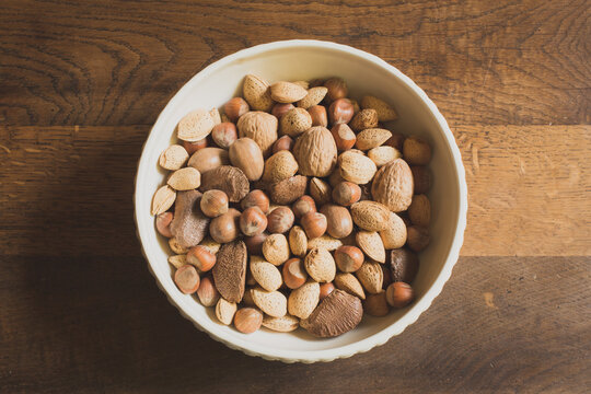 Overhead view of white bowl of mixed nuts centered on a vintage wooden table with copy space