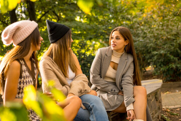 Women friends sitting talking in a park in autumn at sunset, lifestyle and autumnal outfit