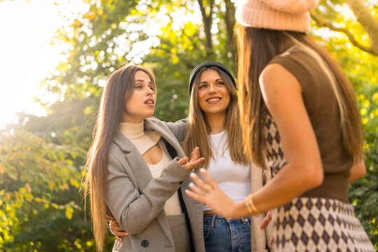 Women Friends Talking In A Park In Autumn At Sunset, Golden Hour, Lifestyle And Autumnal Outfit