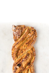 Closeup view of the front part of a delicious braided pastry with raisins, icing sugar and laminated almonds over it on a marbled white background.