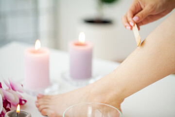 Obraz na płótnie Canvas Woman applies wax to her leg to remove hair