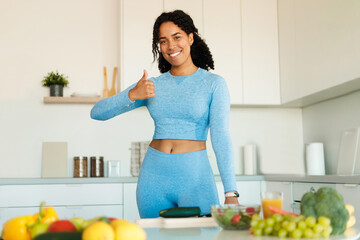 Happy black fitness woman wearing sportswear and showing thumb up while preparing healthy salad in kitchen