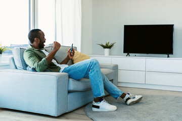 Side view of black guy watching sports game on TV with blank screen, celebrating victory and...