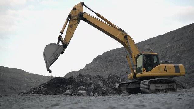 The excavator rakes the ore with the bucket, forming a pile. The action takes place in an open pit. 