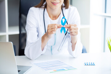 Doctor man holding light Blue Ribbon for supporting people living and illness.