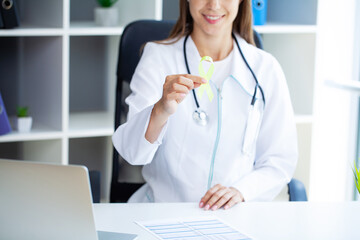 Close up woman in white t-shirt holding and showing yellow awareness ribbon in her hands