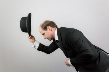 Portrait of Butler in Dark Suit Bowing and Doffing Bowler Hat in Courteous Greeting. Professional...