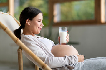 Smiling Young Woman Placing Glass With Milk On Her Pregnant Belly