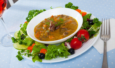 Image of goulash from chicken hearts with vegetables and fresh lettuce served at plate