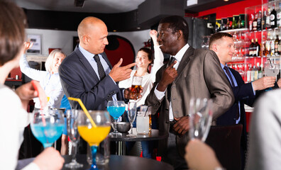 Two glad cheerful smiling male colleagues enjoying corporate bar party, drinking beer and having fun conversation