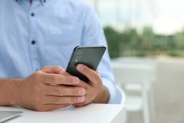 Man using smartphone in outdoor cafe, closeup. Space for text
