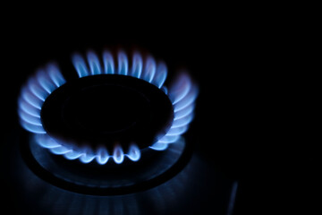 Gas cooktop with burning flame in darkness, closeup. Space for text