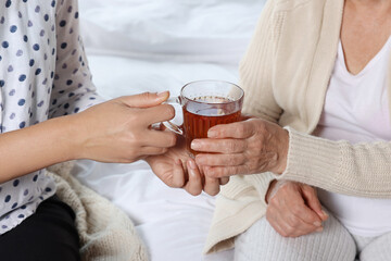 Caregiver giving tea to elderly woman at home, closeup