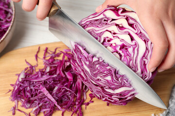 Woman cutting fresh red cabbage at white wooden table, closeup