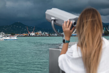 Woman looking through mounted binoculars at mountains. Space for text