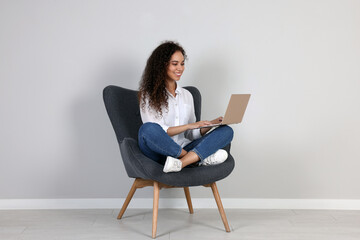 Young African-American woman working on laptop in armchair indoors