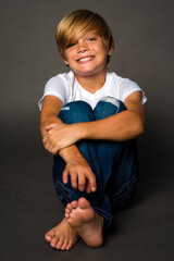 Portrait of a blond haired boy sitting and smiling in blue jeans and a t-shirt © 3Days2Go Media