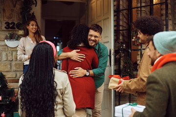 Happy man embracing one of friends while welcoming guests with his wife at the doorstep.