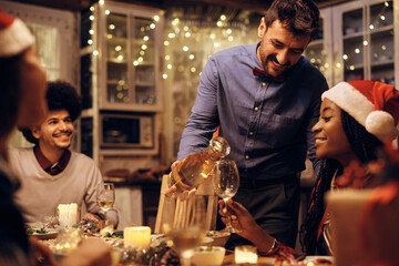 Happy man serving wine to his friends during dinner party on Christmas.