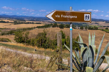 Landscape along via Francigena with Mud road, fields, trees and vineyard.  Sign showing the...