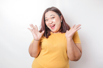 A portrait of a shocked big sized Asian woman wearing a yellow t-shirt, isolated by a white...