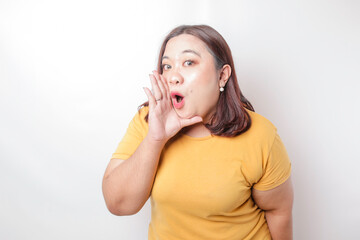Young beautiful Asian big sized woman wearing a yellow shirt shouting and screaming loud with a...
