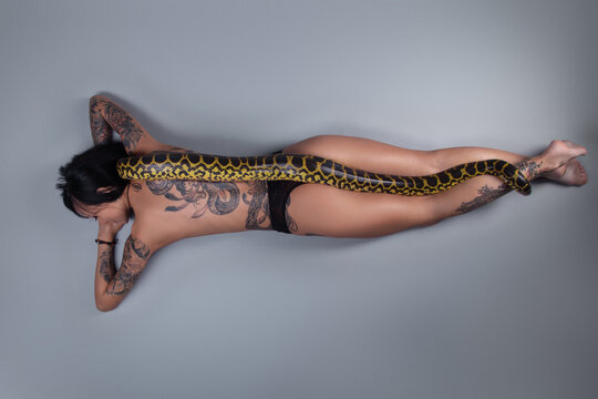 Photo of the topless woman lying on the floor and snake on her spine