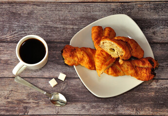 A cup of hot black coffee, two sugar cubes and a plate of layered spiral buns on a wooden table.