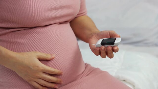 close up of pregnant woman checking blood sugar level by herself with glucose meter at home. gestational diabetes concept