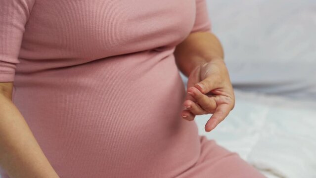 close up of pregnant woman checking blood sugar level by herself with glucose meter at home. gestational diabetes concept.