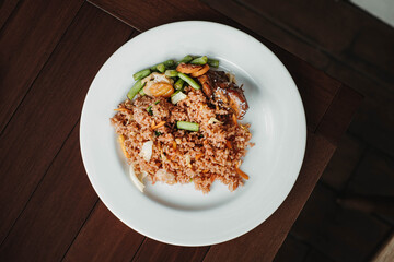 Flat lay or top view shot of a plate of fried rice with egg, vegetables and roasted chicken in the wooden table