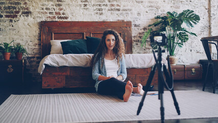 Attractive young woman with long curly hair blogger is recording video for her internet blog using camera.